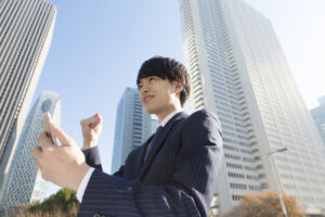 スマホを見て　ガッツポーズ　ビジネスマン　屋外　青空　高層ビル街　就活汎用
